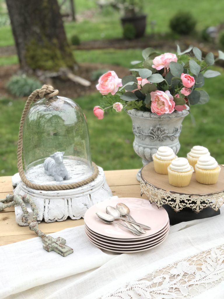 Vanilla Lavender Cupcakes Filled with Lemon Buttercream Frosting stack of pink plates with silver spoons on top. cake tray with 4 white cupcakes. a urn filledwith pink flowers and a glass jar on a pedestal