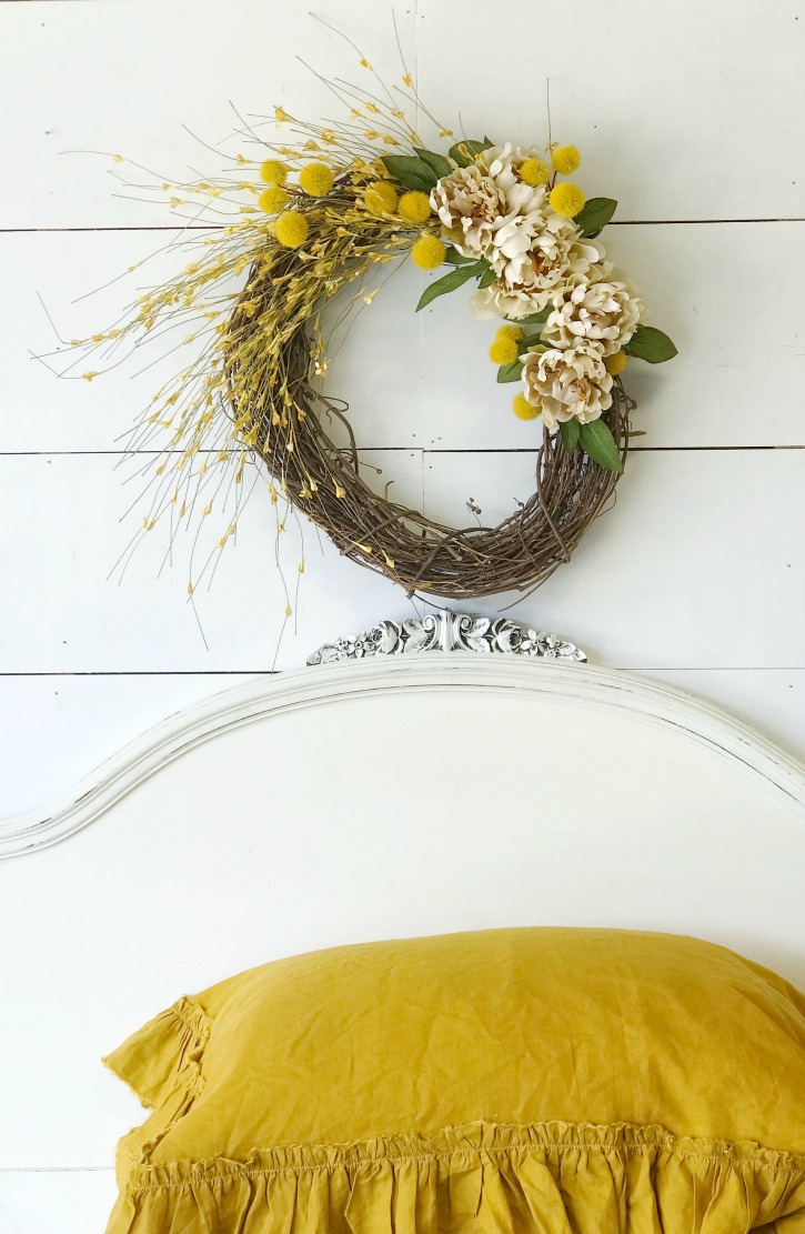 How to Make a Fall Wreath for Your Home with wreath aove white headboard and 2 yellow linen pillows stacked